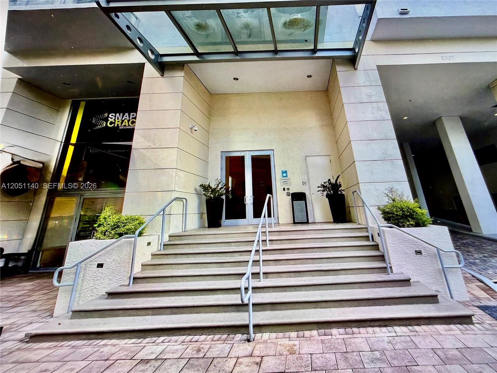 Exterior view of a building entrance featuring concrete stairs, metal railings, and a glass canopy — 1050 Brickell Ave # 2018, Miami FL 33131, MIAMI, FL