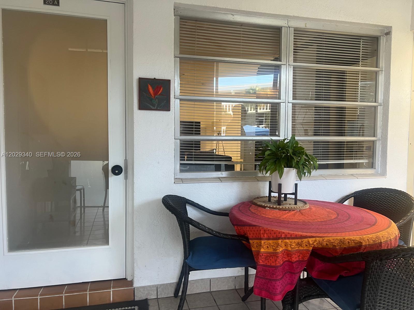 A patio features a small round table with a colorful cloth, chairs, and a potted plant — 181 NE 14th Ave # 20A, Hallandale Beach FL 33009, HALLANDALE BEACH, FL