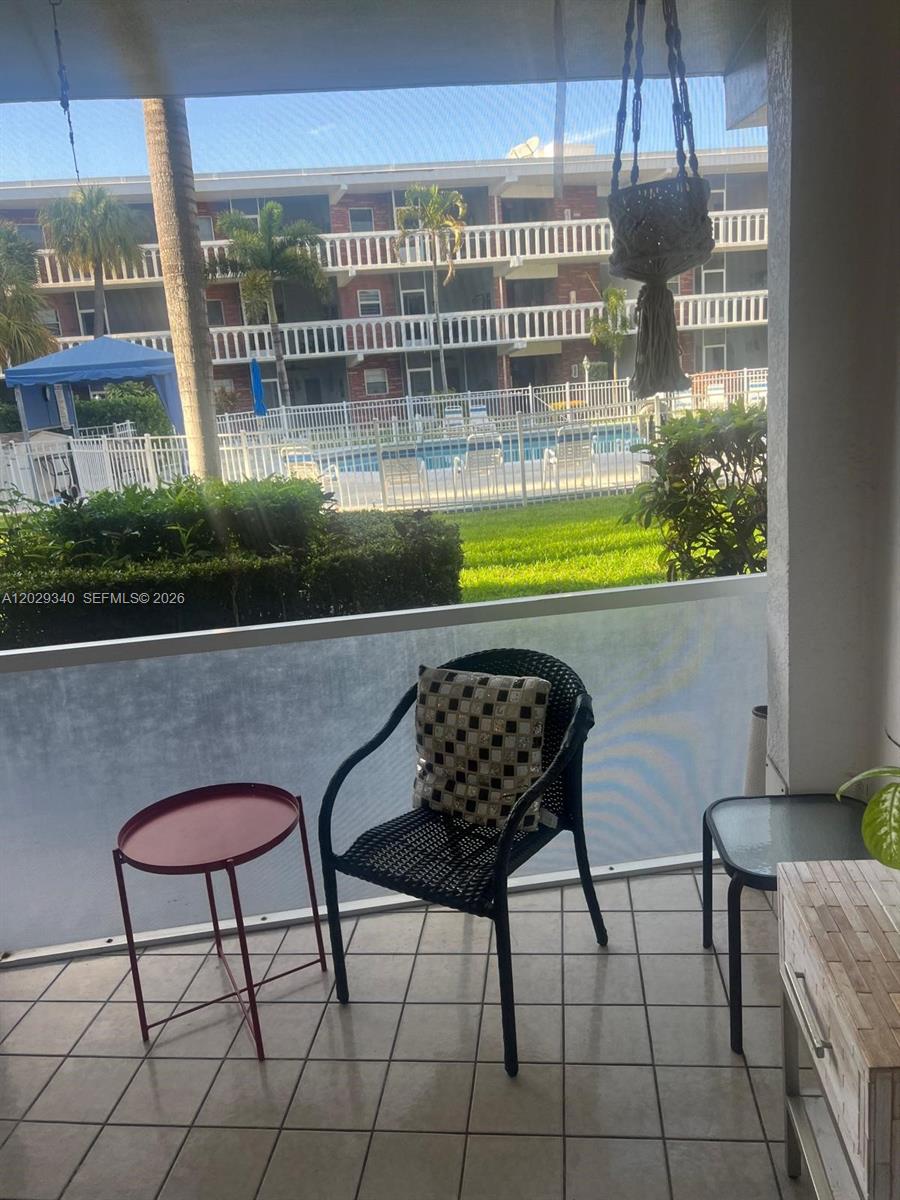 A screened-in patio features tiled flooring, a black wicker chair, and a pool view — 181 NE 14th Ave # 20A, Hallandale Beach FL 33009, HALLANDALE BEACH, FL
