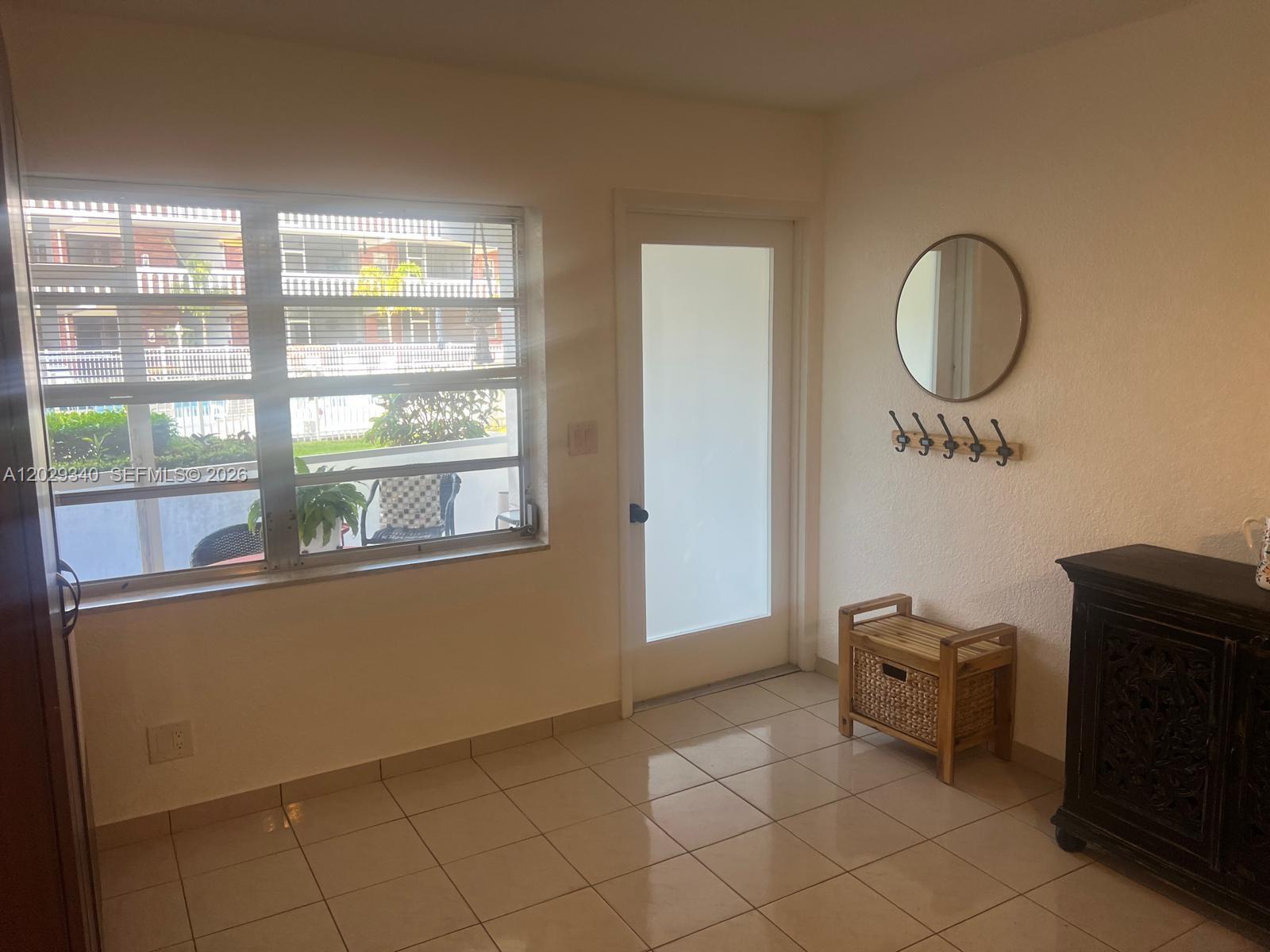 A bright room features tiled floors, a large window, a glass door, and wall-mounted decor — 181 NE 14th Ave # 20A, Hallandale Beach FL 33009, HALLANDALE BEACH, FL