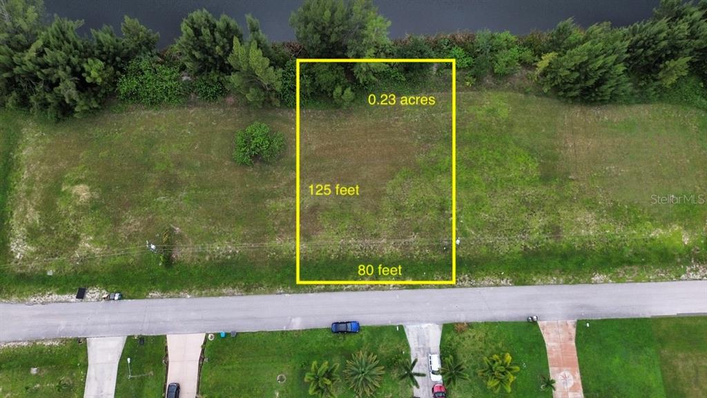 An aerial view shows a rectangular vacant lot outlined in yellow next to a canal — 426 NE 20TH STREET, CAPE CORAL, FL