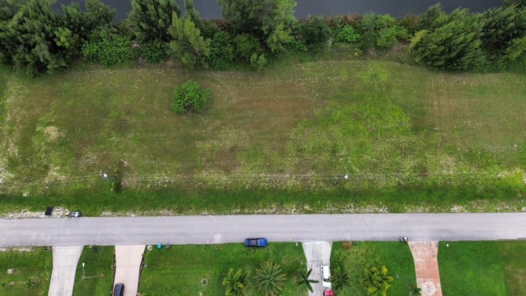 An aerial view shows a vacant, grassy residential lot bordering a canal and a road — 426 NE 20TH STREET, CAPE CORAL, FL