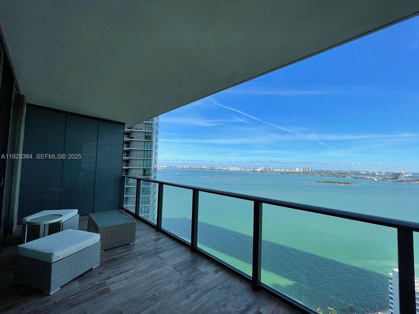 A balcony with outdoor furniture overlooks a large body of water and a distant city skyline — 650 NE 32nd St # 3005, Miami FL 33137, MIAMI, FL