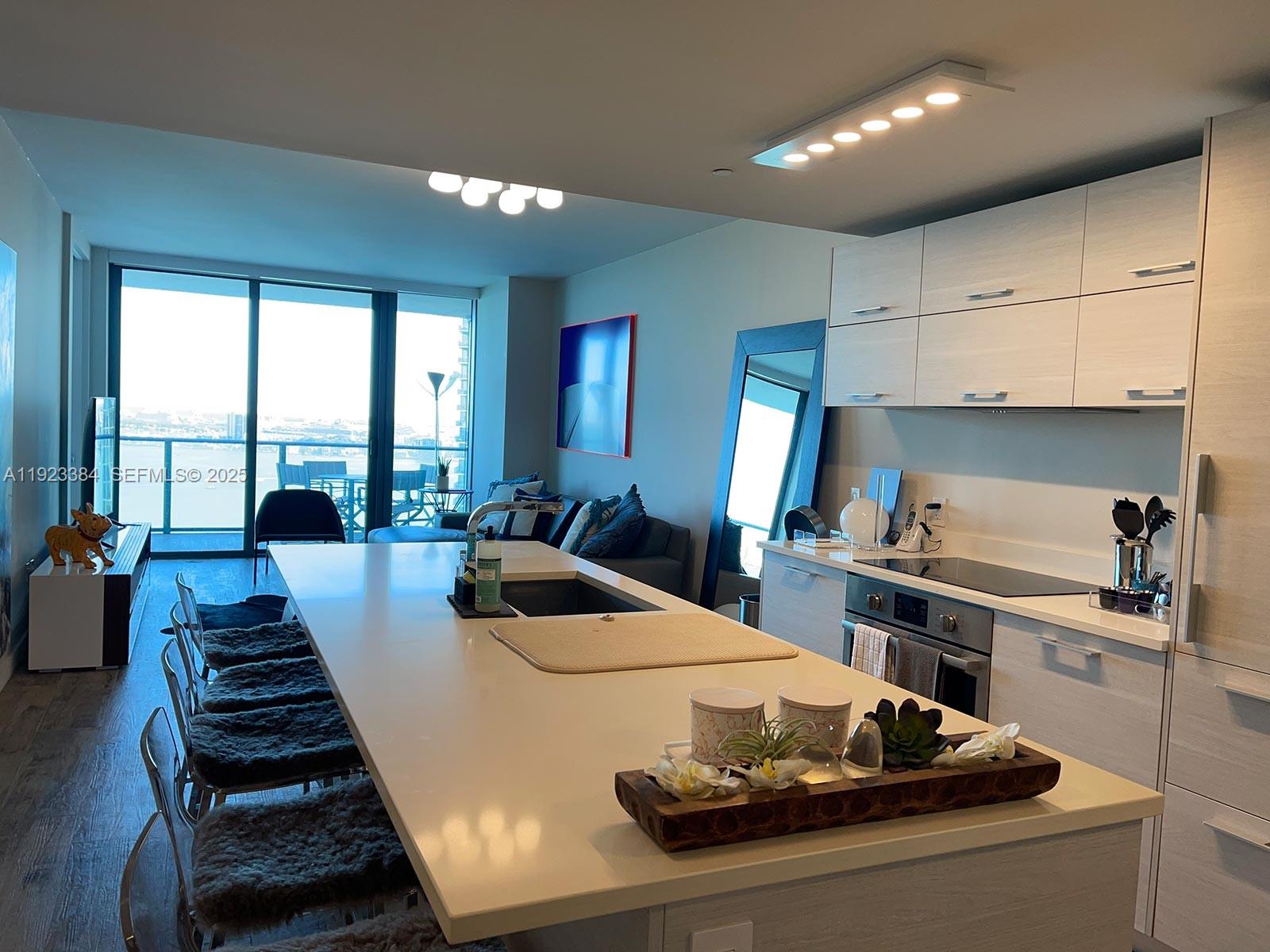 A modern kitchen with a large white island overlooks a living area and balcony — 650 NE 32nd St # 3005, Miami FL 33137, MIAMI, FL