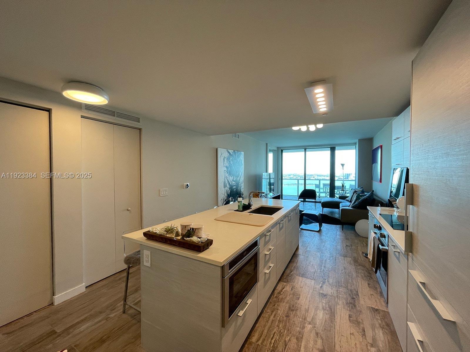 A modern kitchen with a central island overlooks a living area and a waterfront balcony — 650 NE 32nd St # 3005, Miami FL 33137, MIAMI, FL