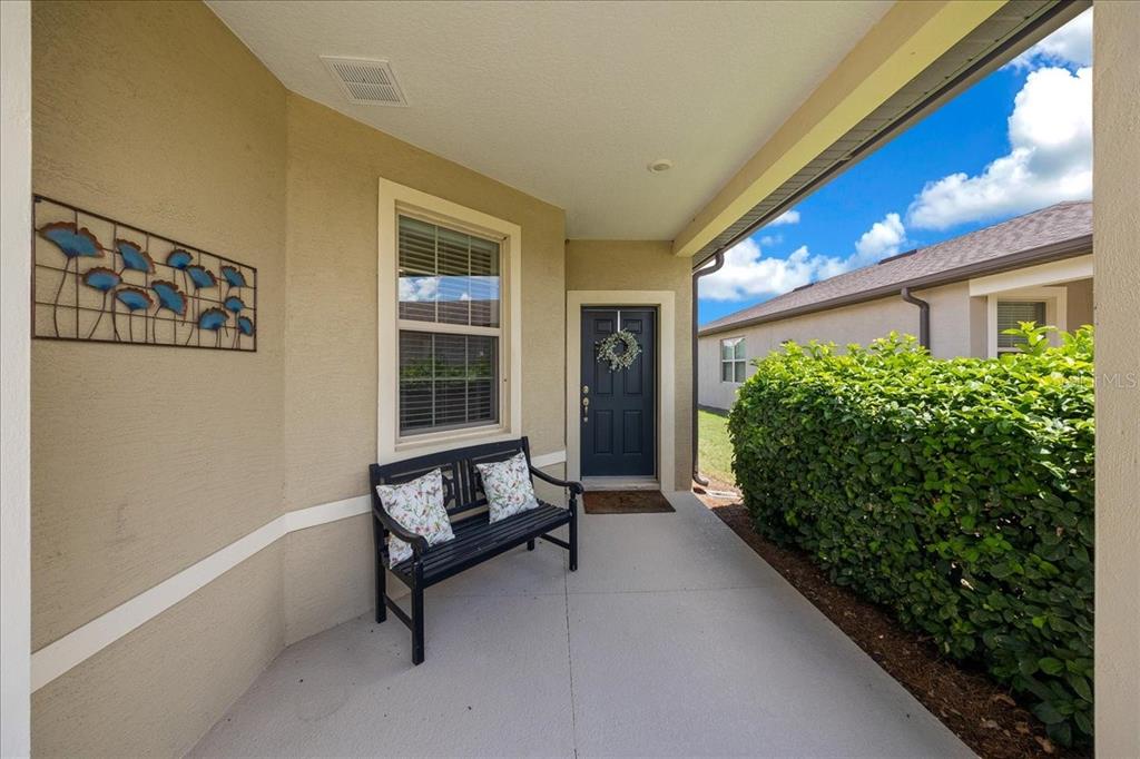 A covered entryway features a black bench, a dark front door, and a large hedge — 9645 SW 63RD LOOP, OCALA, FL
