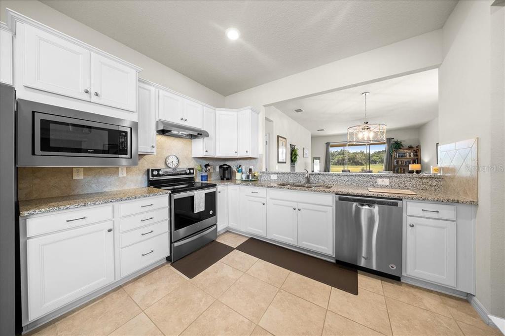 A kitchen features white cabinets, granite countertops, stainless steel appliances, and tile flooring — 9645 SW 63RD LOOP, OCALA, FL