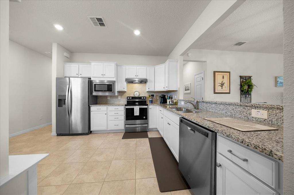 A kitchen with white cabinets, granite countertops, stainless steel appliances, and light-colored tile flooring — 9645 SW 63RD LOOP, OCALA, FL