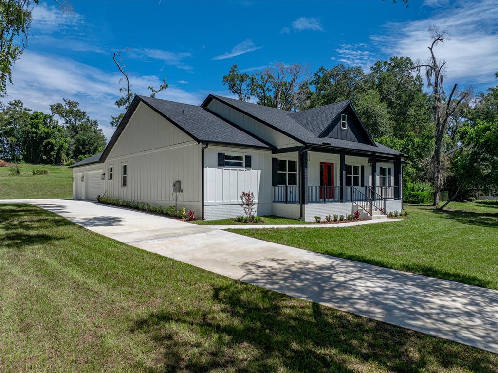 A white farmhouse-style house with a black roof, red front door, and a concrete driveway — 14069 GRANDEUR WAY, DADE CITY, FL