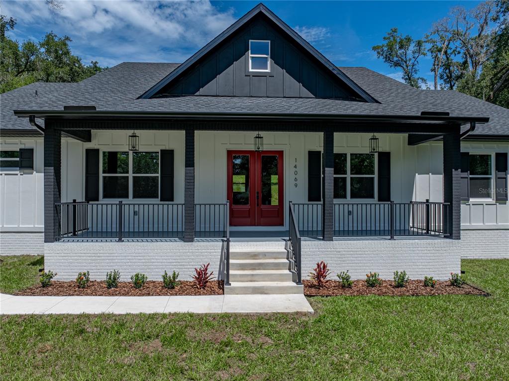 A modern farmhouse with a white brick base, black trim, and a bright red front door — 14069 GRANDEUR WAY, DADE CITY, FL