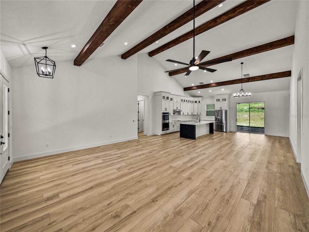 An open-concept living area features vaulted ceilings with exposed wood beams and light wood flooring — 14069 GRANDEUR WAY, DADE CITY, FL