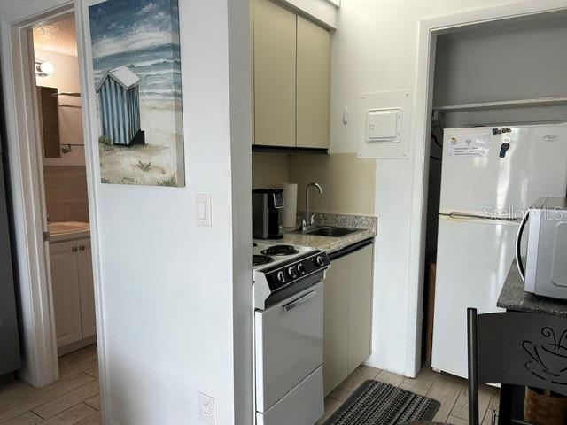 A small kitchen features white cabinets, a stove, a refrigerator, and an adjacent bathroom doorway — 908 VILLAS DRIVE UNIT 68, VENICE, FL