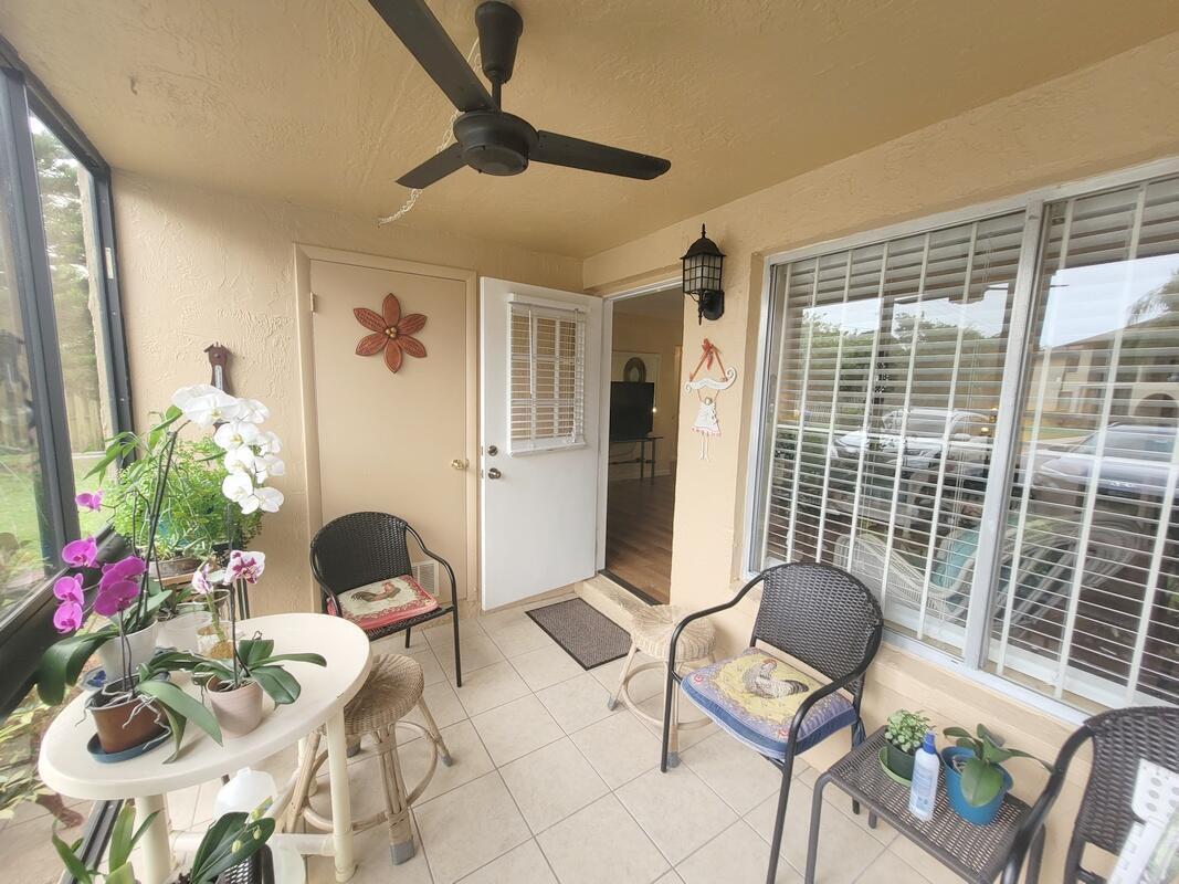 A covered patio features tiled flooring, a ceiling fan, two wicker chairs, and potted orchids — 320 Pine Ridge Circle # A1, FL 33463, FL