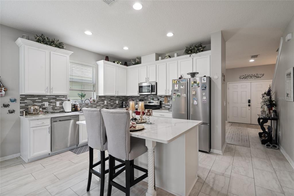 A kitchen features white cabinets, stainless steel appliances, a marble-topped island, and light tile flooring — 12532 SAWGRASS OAK STREET, ORLANDO, FL