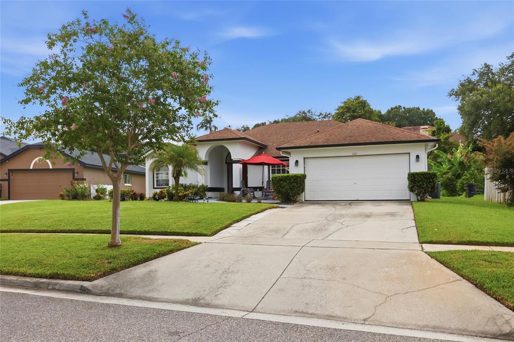 A single-story house with a white garage, a red patio umbrella, and a large front tree — 1331 COUNTRYRIDGE PLACE, ORLANDO, FL