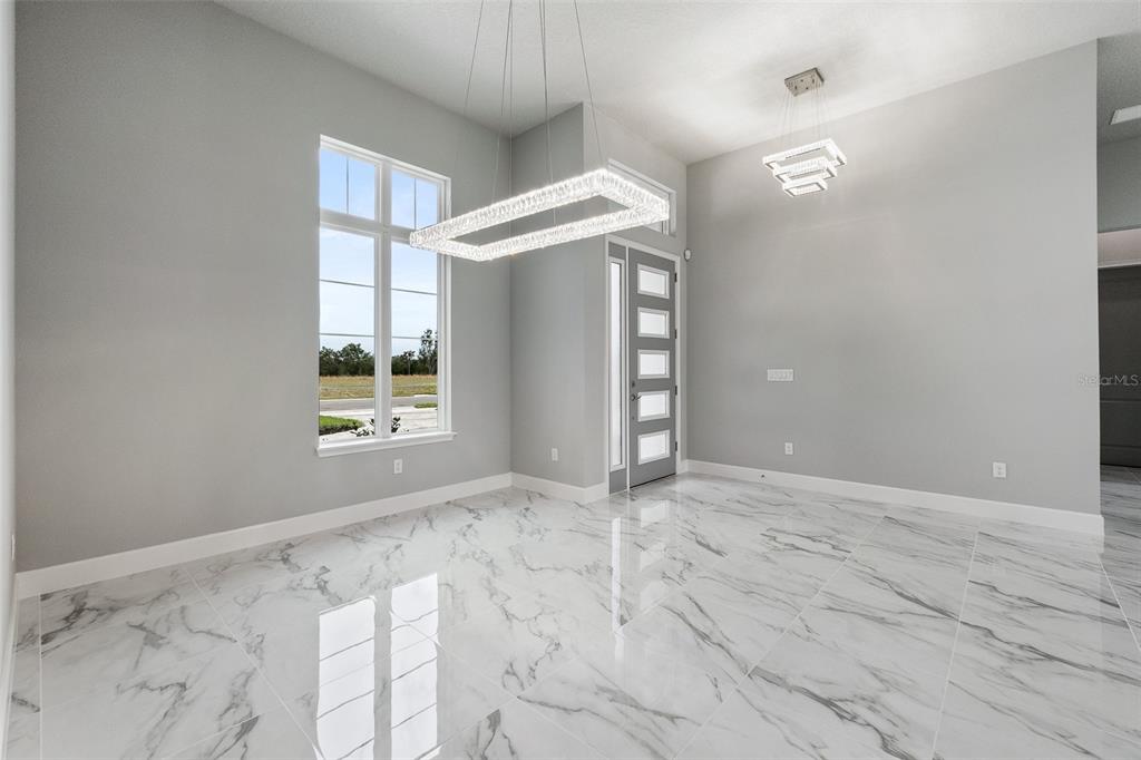 A bright dining area features marble-look tile flooring, two modern crystal chandeliers, and a front door — 29 CORONADO ROAD, FLAGLER BEACH, FL