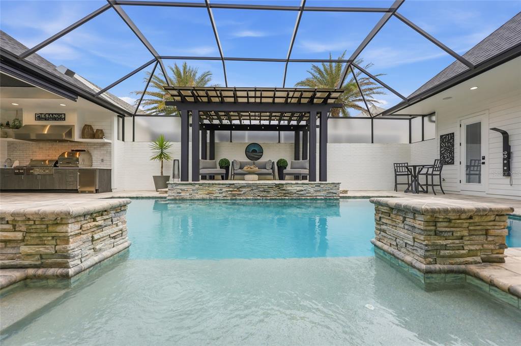 A screened-in patio features a swimming pool, a stone-accented pergola, and an outdoor kitchen — 1045 SW 132 STREET, NEWBERRY, FL