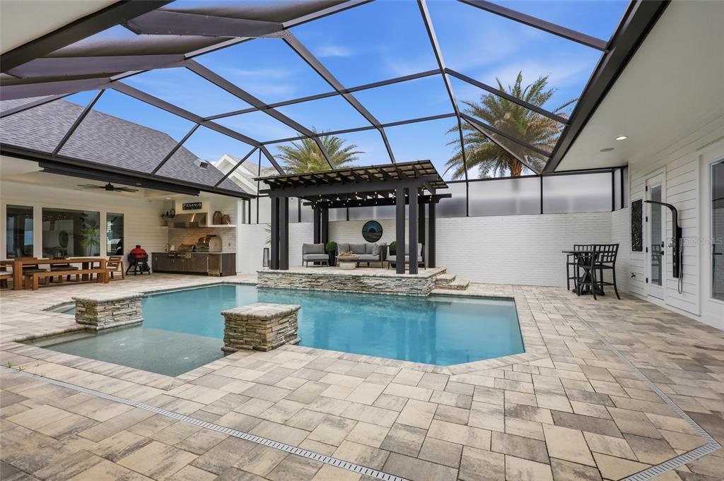A screened-in patio features a swimming pool, a raised pergola seating area, and outdoor kitchen — 1045 SW 132 STREET, NEWBERRY, FL