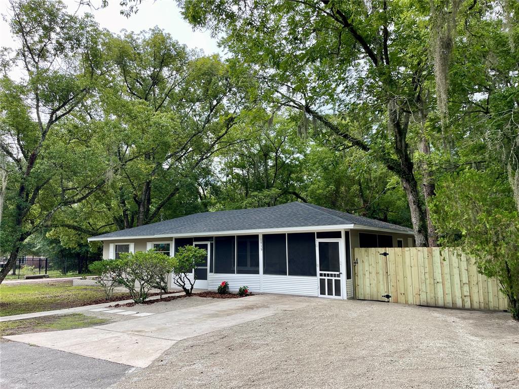 A single-story house with a screened-in porch, a gravel driveway, and surrounding mature trees — 1715 NE 6TH PLACE, GAINESVILLE, FL