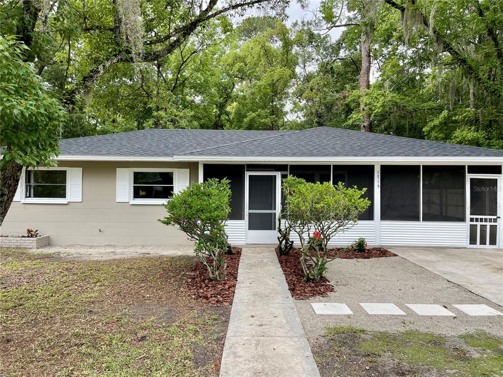 A single-story house with a beige exterior, white shutters, and a screened-in front porch — 1715 NE 6TH PLACE, GAINESVILLE, FL