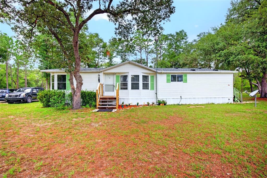 A single-story manufactured home with white siding, green shutters, and a wooden front porch — 10890 NE 102ND PLACE, ARCHER, FL