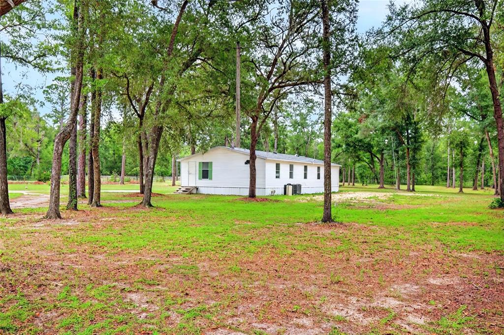 A white mobile home sits on a grassy, tree-filled lot under a cloudy sky — 10890 NE 102ND PLACE, ARCHER, FL
