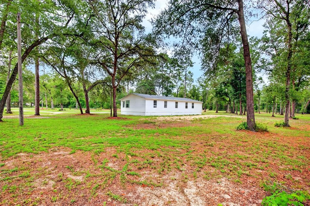 A white mobile home sits on a large, grassy lot surrounded by mature trees — 10890 NE 102ND PLACE, ARCHER, FL