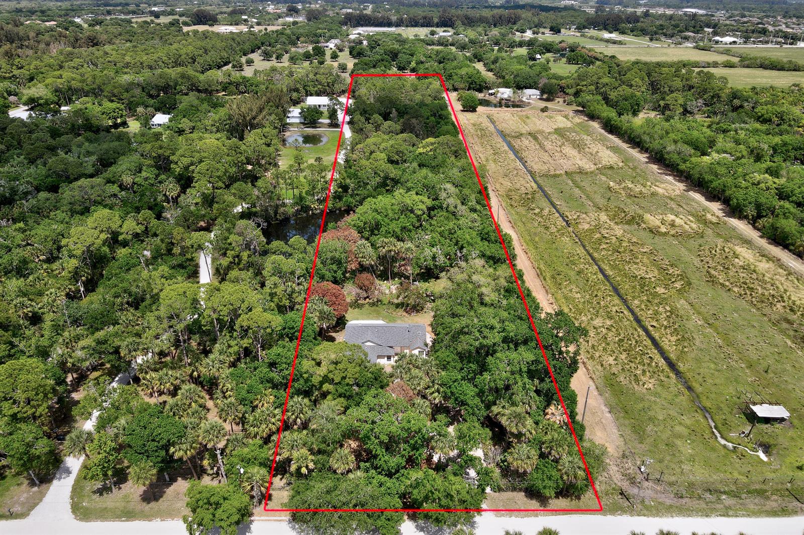 An aerial view shows a house situated on a large, wooded lot outlined in red — 6930 41st Street, Vero Beach FL 32967, VERO BEACH, FL