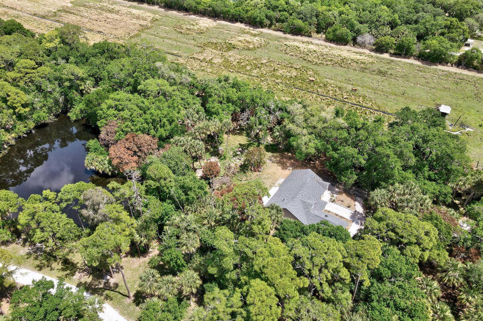 An aerial view shows a house surrounded by dense trees and a pond near pasture — 6930 41st Street, Vero Beach FL 32967, VERO BEACH, FL