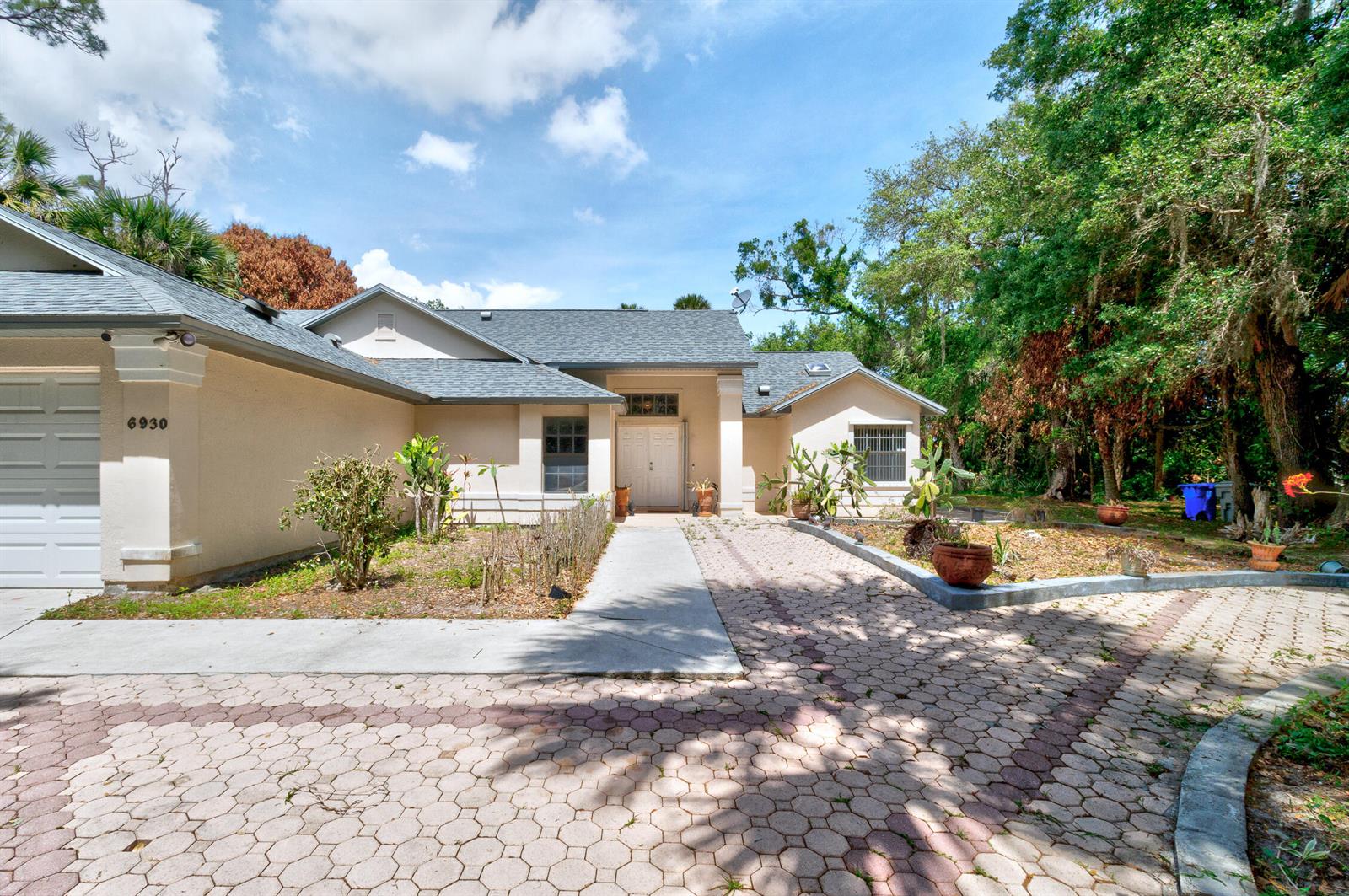 A single-story house with a paved driveway, tan stucco exterior, and a gray shingled roof — 6930 41st Street, Vero Beach FL 32967, VERO BEACH, FL
