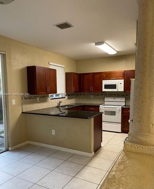 A kitchen features dark wood cabinets, black countertops, white appliances, and light-colored tile flooring — 6970 NW 177th St # M104, Hialeah FL 33015, HIALEAH, FL