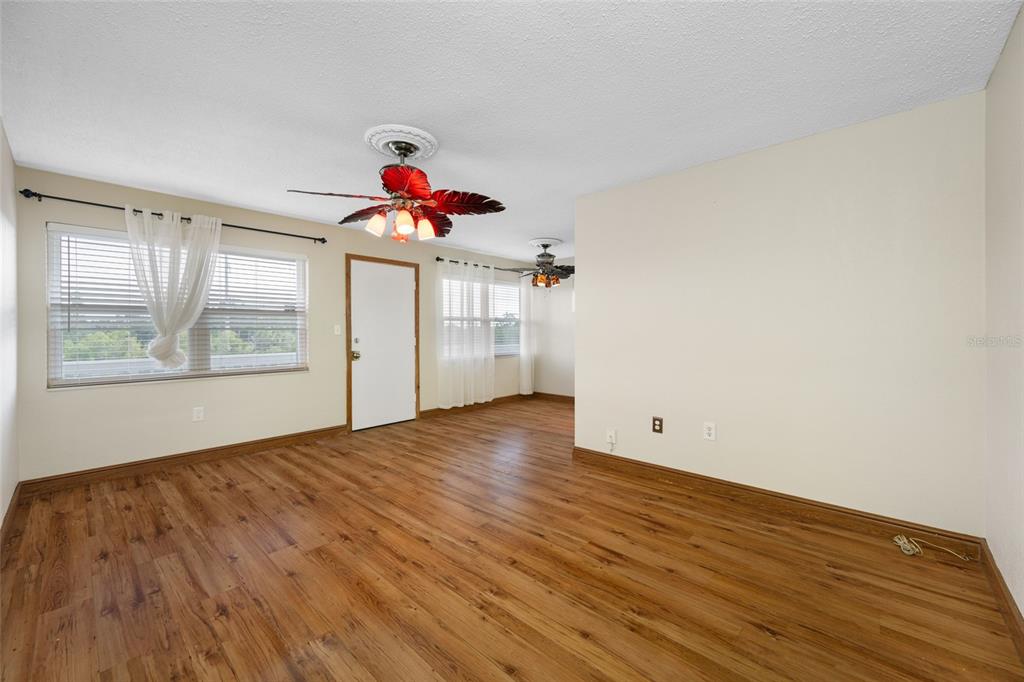 An empty room with wood-look flooring, two ceiling fans, and windows with white curtains — 1001 77TH AVENUE N UNIT 308, ST PETERSBURG, FL