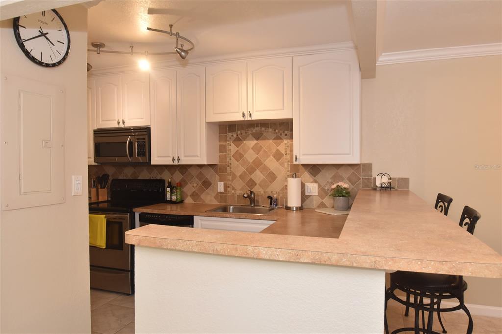A kitchen features white cabinets, a tiled backsplash, stainless steel appliances, and a breakfast bar — 3700 S OSPREY AVENUE UNIT 315, SARASOTA, FL