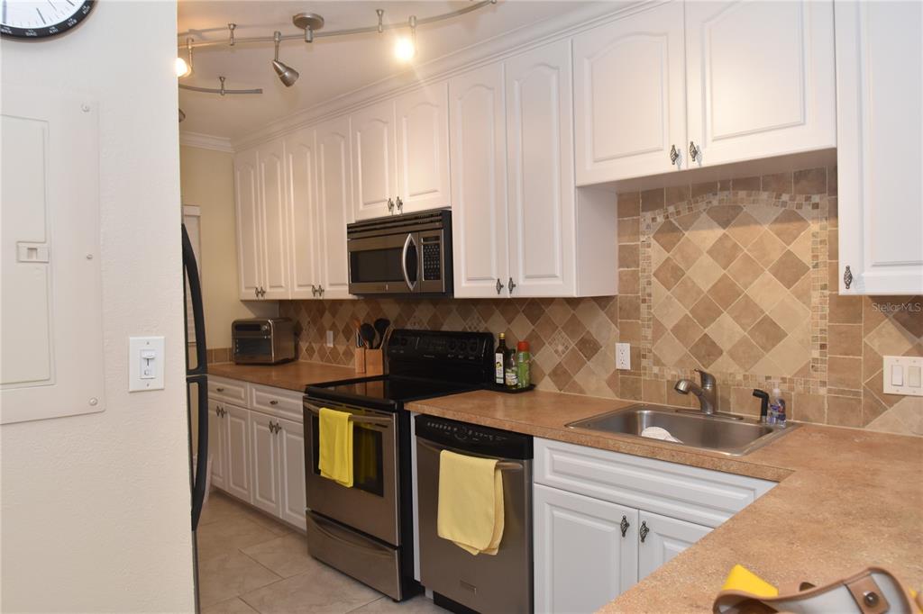 A kitchen features white cabinets, stainless steel appliances, tan countertops, and a tiled backsplash — 3700 S OSPREY AVENUE UNIT 315, SARASOTA, FL