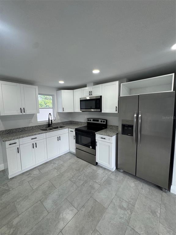 A kitchen features white cabinets, granite countertops, stainless steel appliances, and gray tile flooring — 6840 RUNNEL DRIVE, NEW PORT RICHEY, FL
