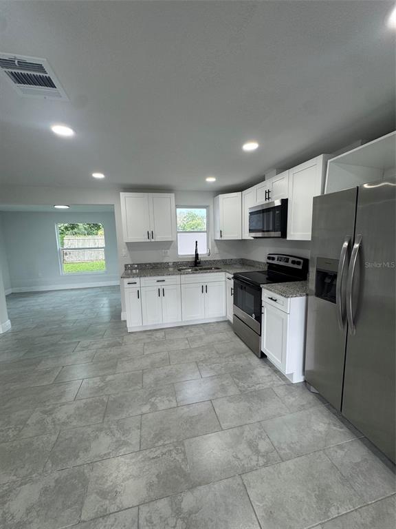 A kitchen with white cabinets, granite countertops, stainless steel appliances, and gray tile flooring — 6840 RUNNEL DRIVE, NEW PORT RICHEY, FL