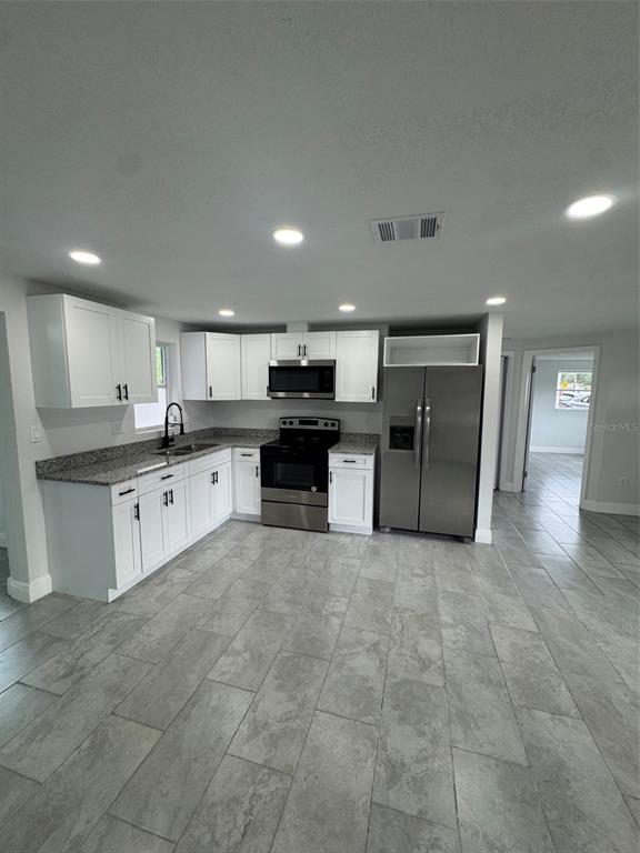 A kitchen features white cabinets, granite countertops, stainless steel appliances, and gray tile flooring — 6840 RUNNEL DRIVE, NEW PORT RICHEY, FL