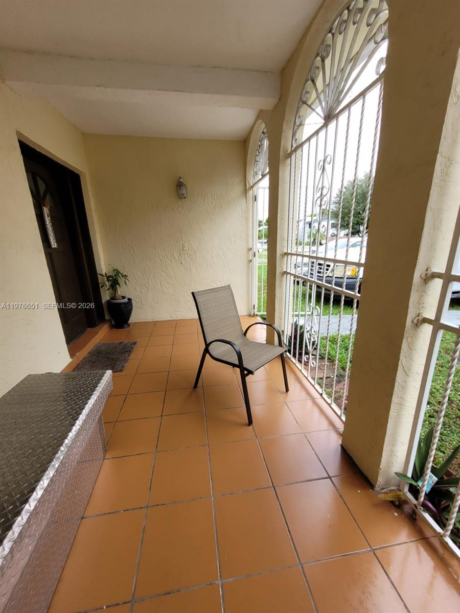 A covered patio features orange tile flooring, a single chair, and a white metal gate — 10932 SW 25th St, Miami FL 33165, MIAMI, FL