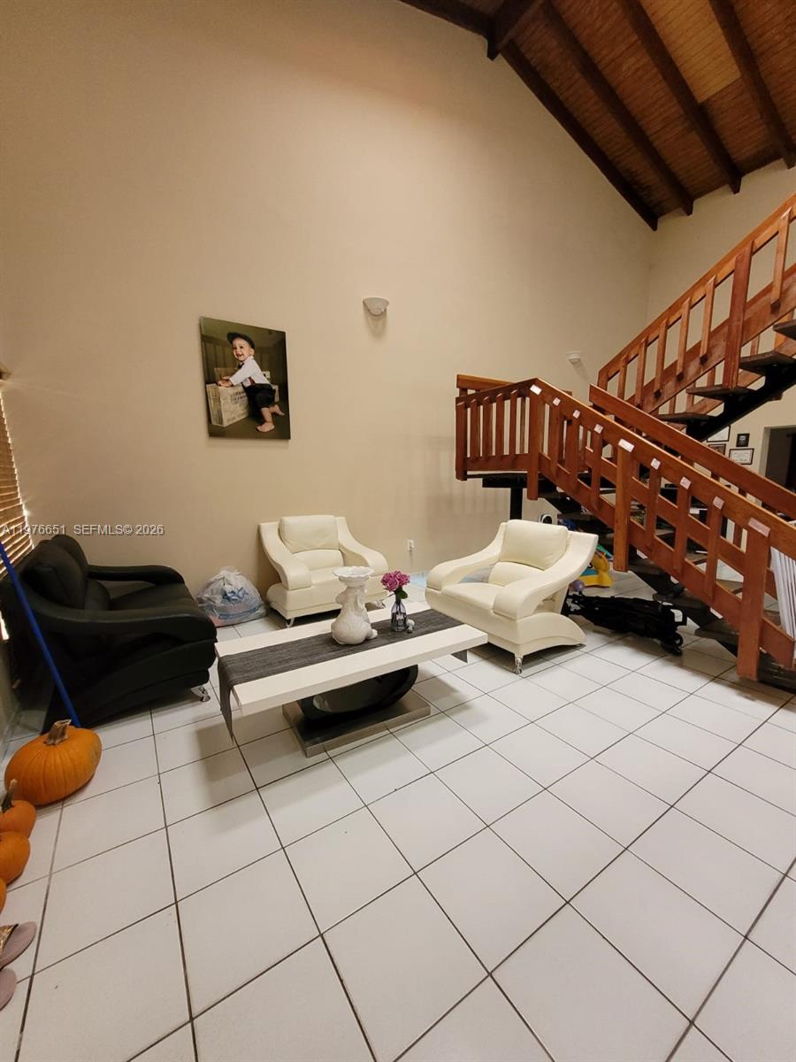 A living room features white tile floors, a wooden staircase, and modern seating furniture — 10932 SW 25th St, Miami FL 33165, MIAMI, FL
