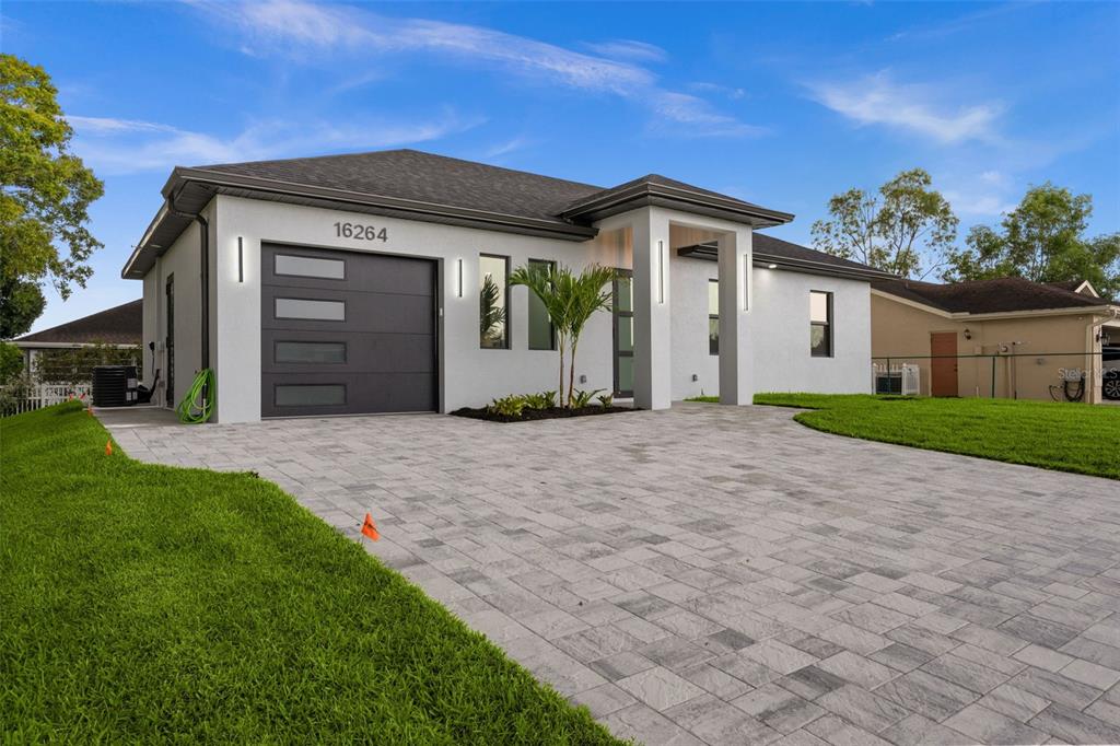 A modern single-story house features a gray garage door, white stucco walls, and paved driveway — 16264 HORIZON ROAD, NORTH FORT MYERS, FL