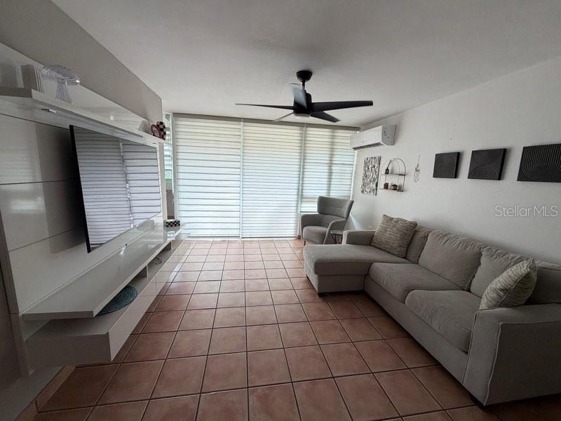 A living room features a large sectional sofa, a wall-mounted television, and tiled flooring — A-500 LAS VILLAS DE CIUDAD JARDIN DEV. UNIT 229, BAYAMON, PR