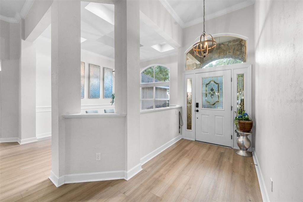 A bright entryway features light wood-look flooring, a white front door, and a spherical chandelier — 9710 SW 33RD LANE, GAINESVILLE, FL