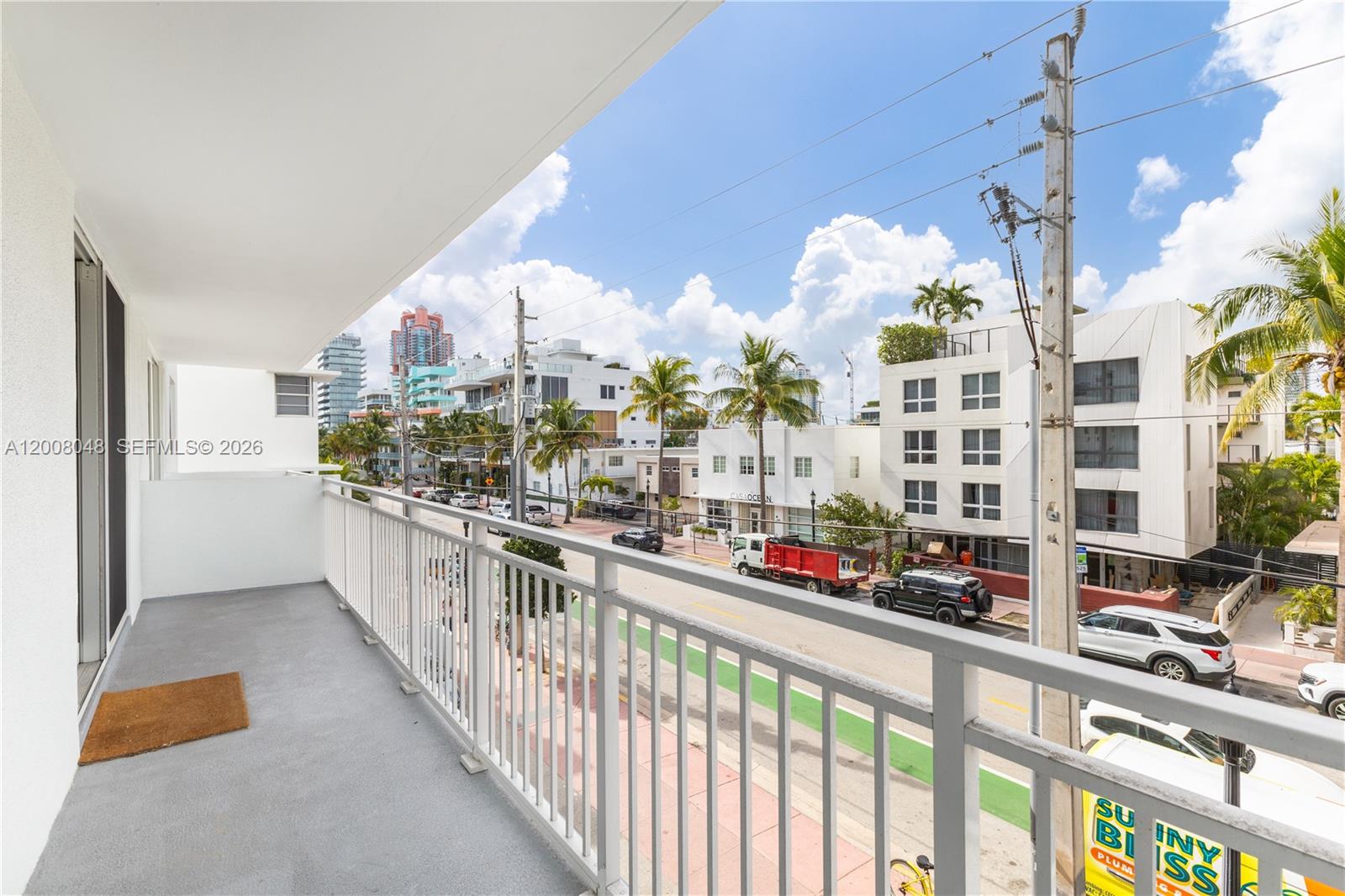 A balcony with a white railing overlooks a street with buildings, palm trees, and vehicles — 345 Ocean Dr # 304, Miami Beach FL 33139, MIAMI BEACH, FL