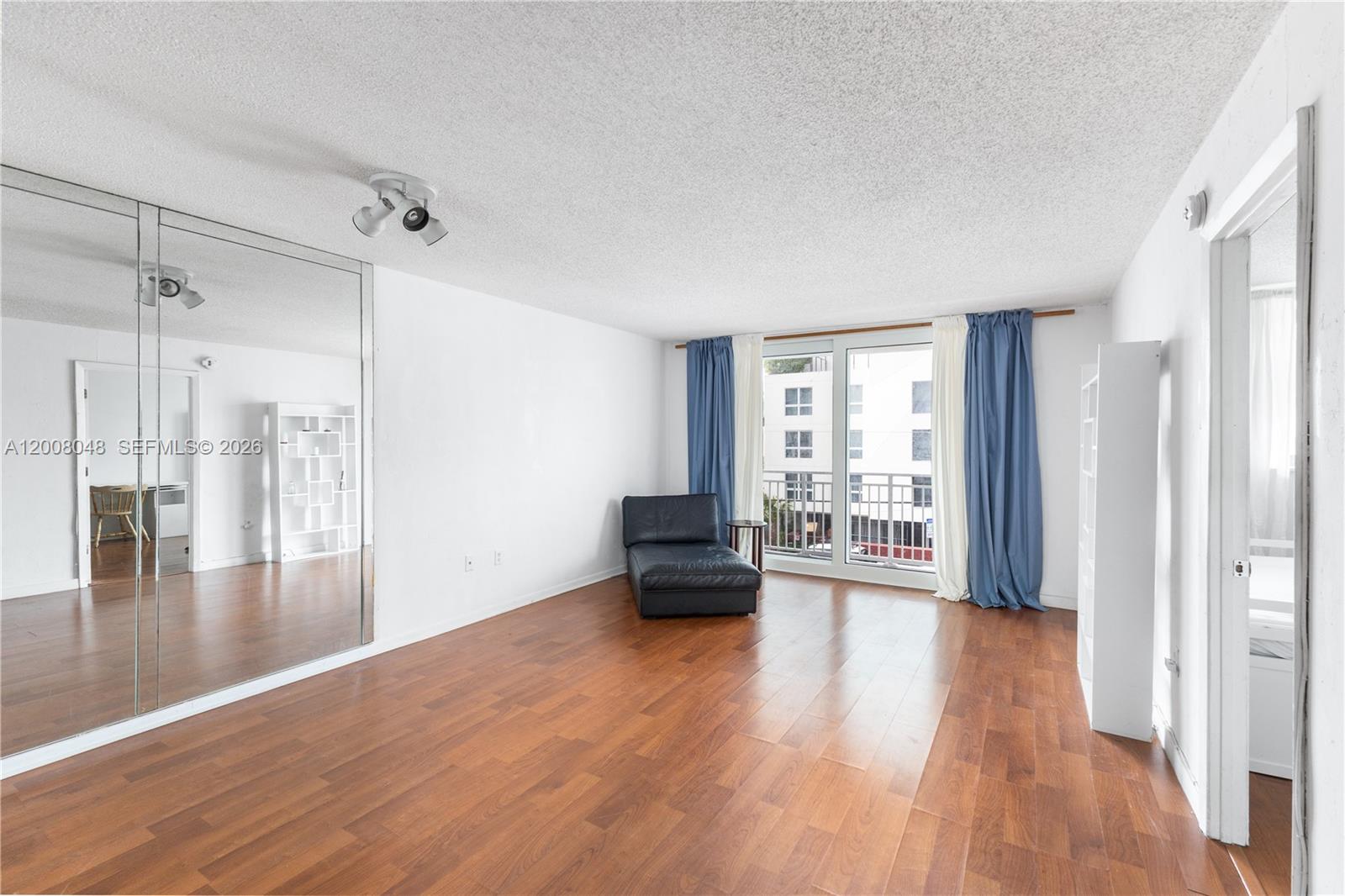 A living room features hardwood floors, a mirrored wall, and a balcony with blue curtains — 345 Ocean Dr # 304, Miami Beach FL 33139, MIAMI BEACH, FL