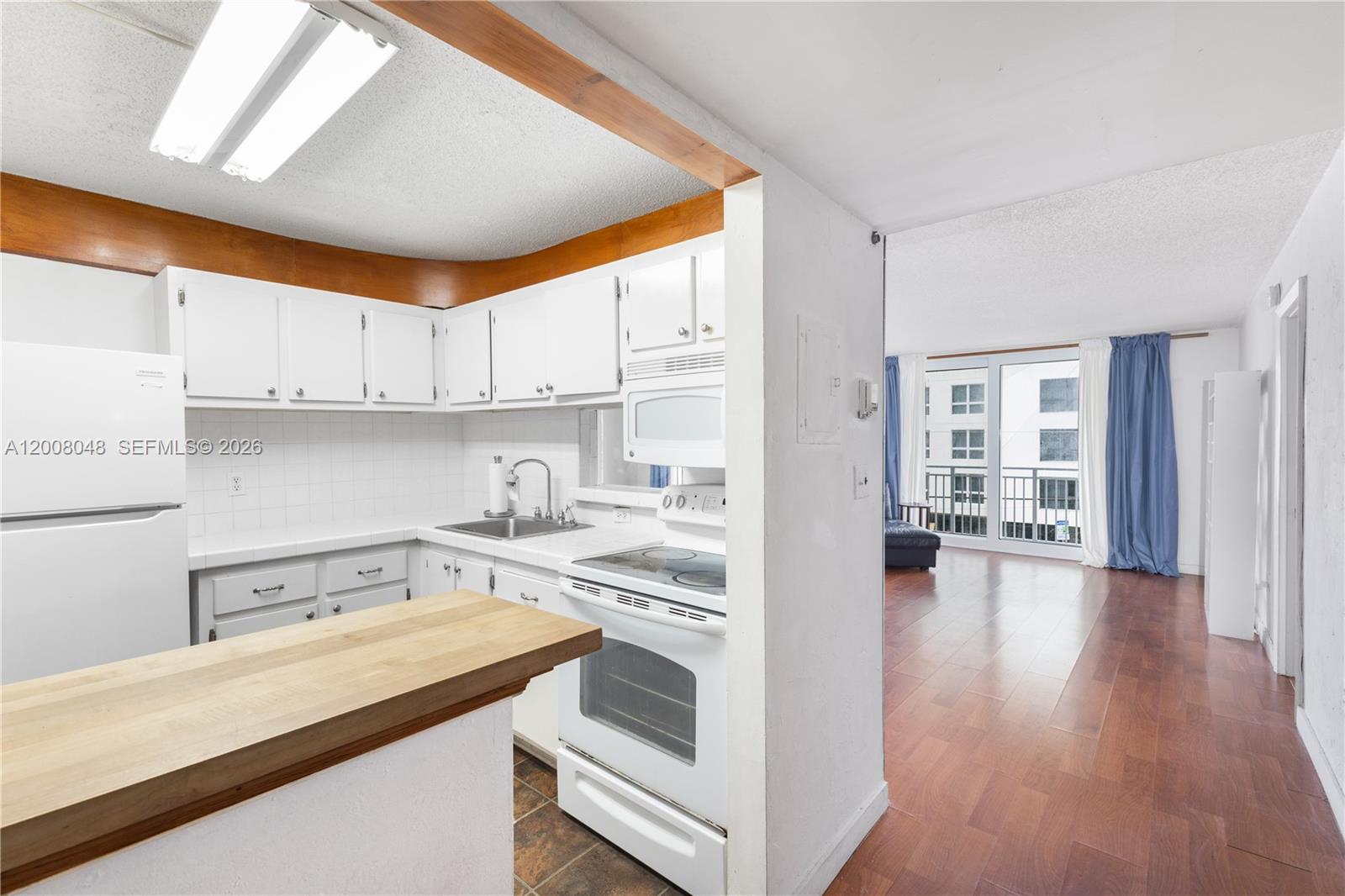A kitchen with white cabinets and appliances opens into a living area with wood flooring — 345 Ocean Dr # 304, Miami Beach FL 33139, MIAMI BEACH, FL