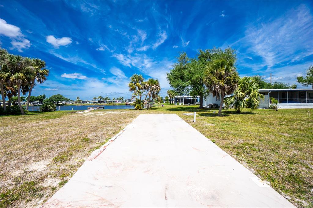 A concrete driveway leads toward a waterfront lot with palm trees and nearby houses — 6371 FALCON DRIVE UNIT 12, ENGLEWOOD, FL