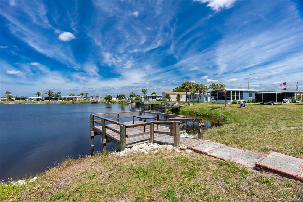 A wooden dock extends into a lake in front of a residential mobile home community — 6371 FALCON DRIVE UNIT 12, ENGLEWOOD, FL