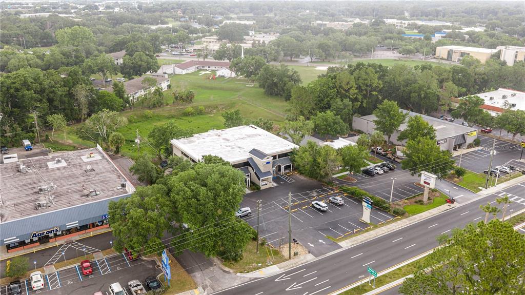 An aerial view shows commercial buildings, parking lots, and surrounding green space near a road — 3101 SW COLLEGE ROAD UNIT 200/204, OCALA, FL