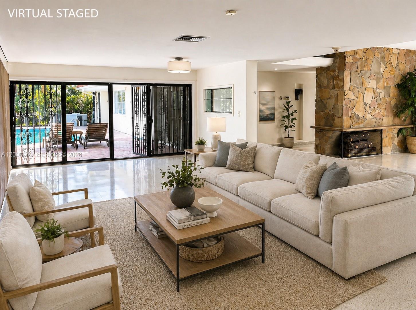 A virtual staged living room features a stone fireplace, light tile floors, and sliding glass doors — 9205 Byron Ave, Surfside FL 33154, SURFSIDE, FL