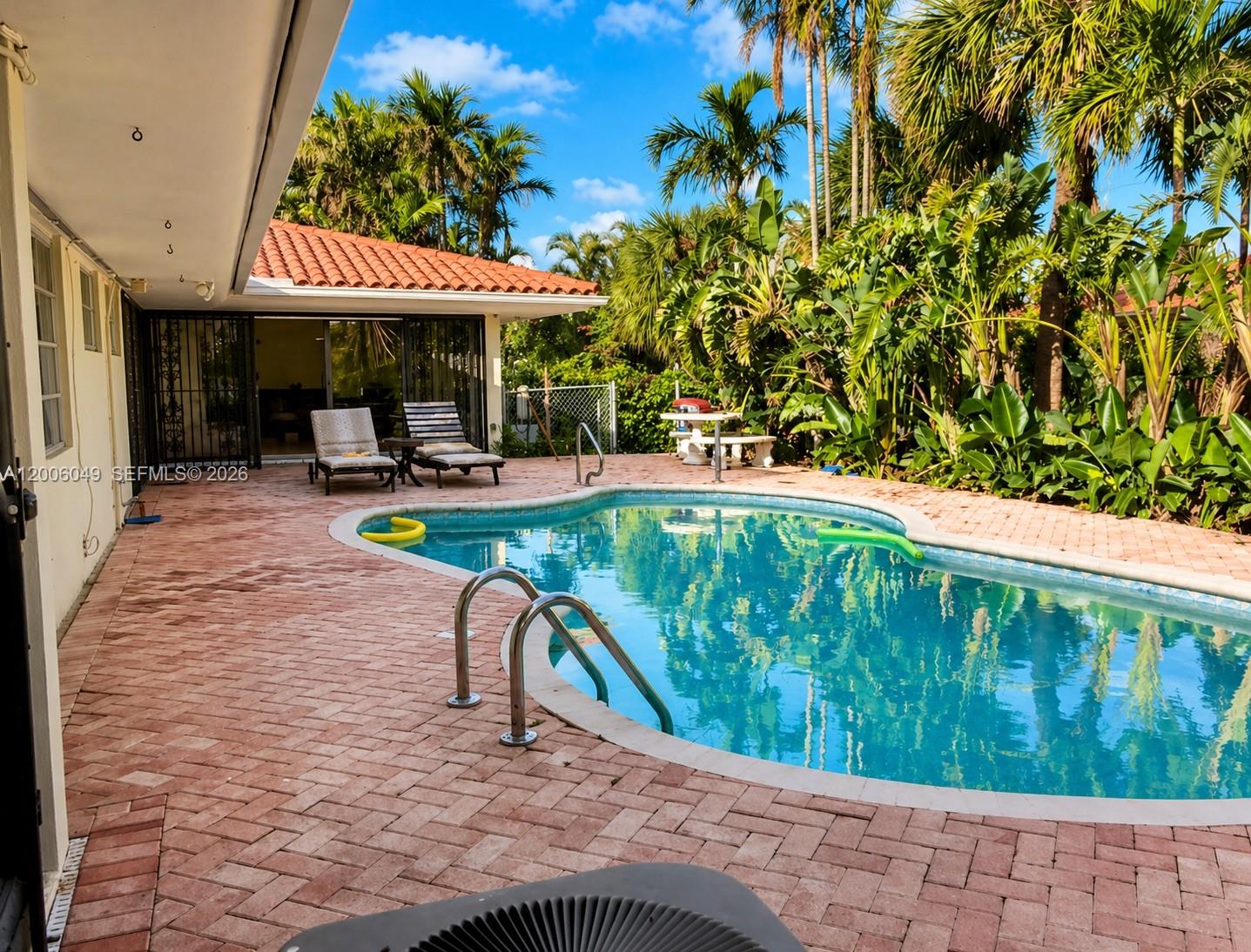 A backyard features a swimming pool, brick patio, lounge chairs, and lush tropical landscaping — 9205 Byron Ave, Surfside FL 33154, SURFSIDE, FL